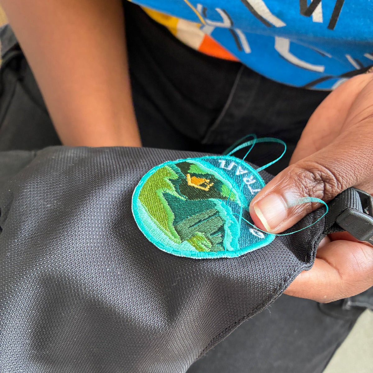person sewing an Otter Trail patch onto backpack