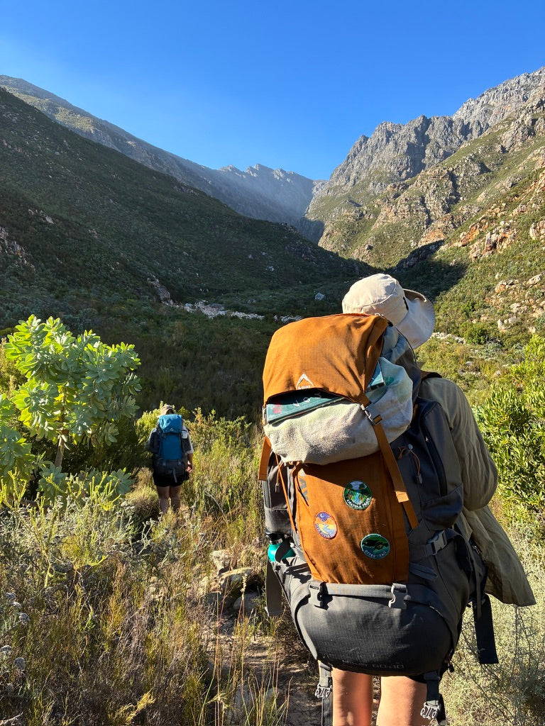 Person hiking with a large backpack covered in patches in a mountainous area of South Africa.