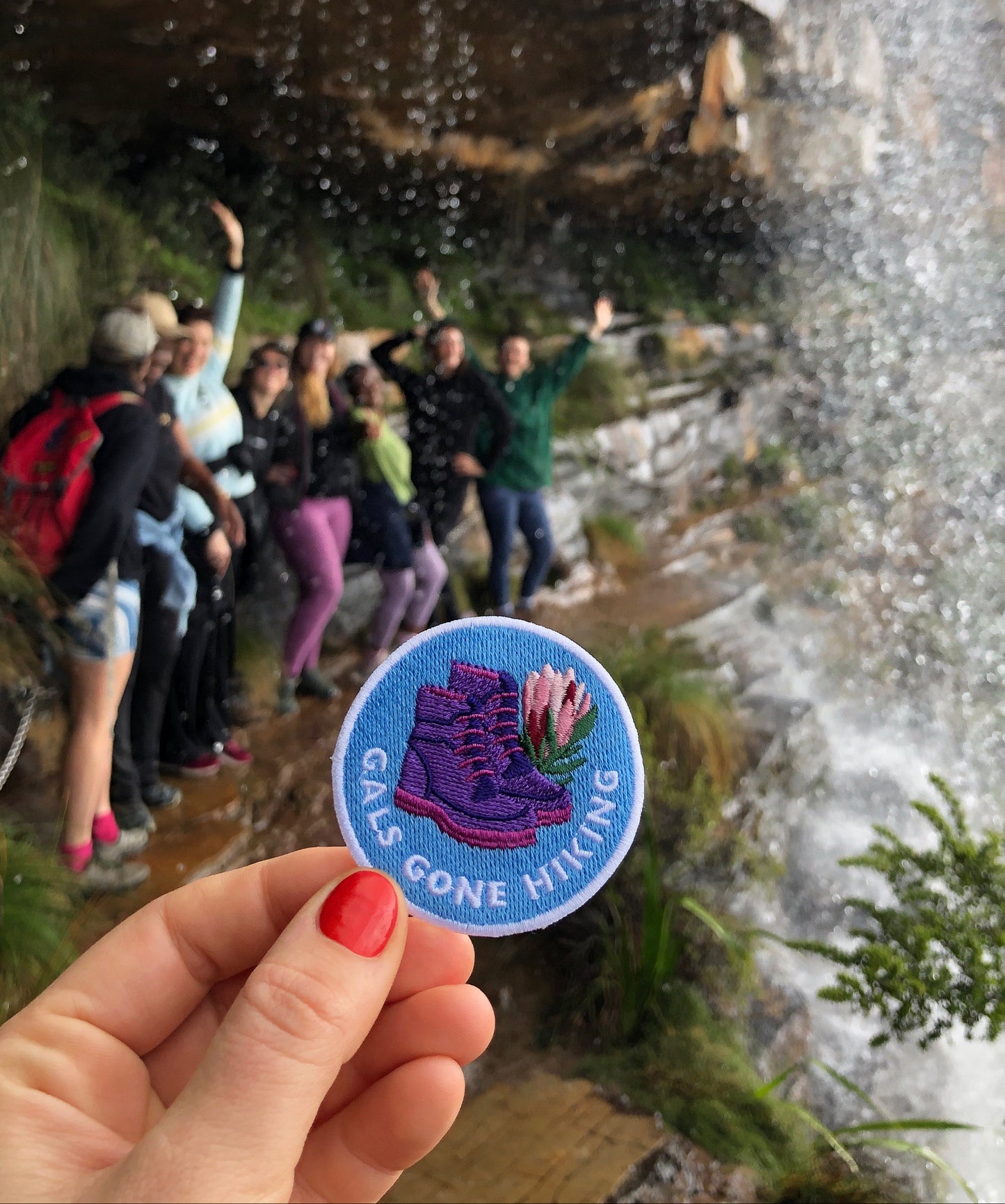 Hikers near a waterfall with a 'Gals Gone Hiking' sticker held in front of the scene.
