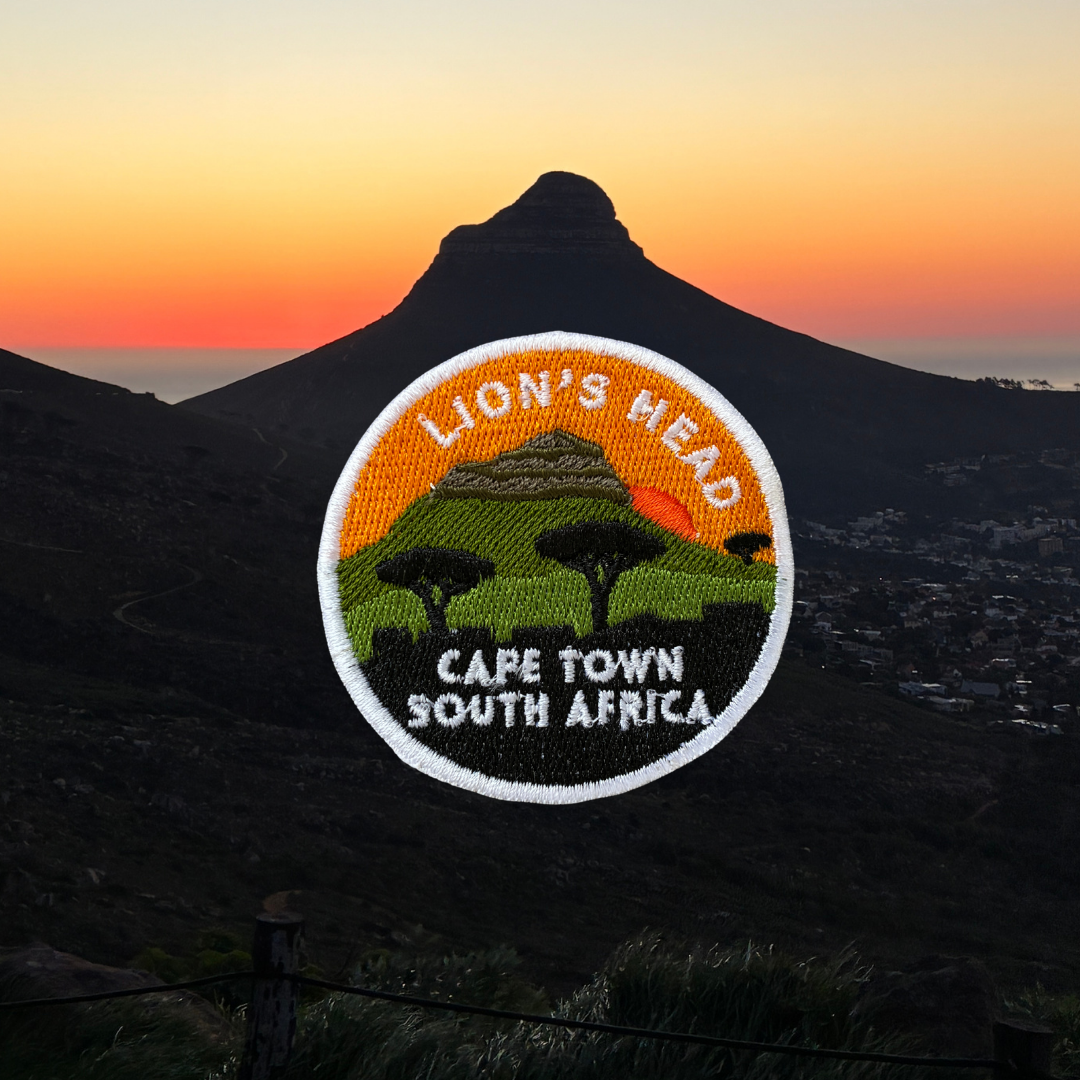 A circular embroidered patch featuring Lion's Head in Cape Town, South Africa, set against a real-world mountain landscape at sunset.