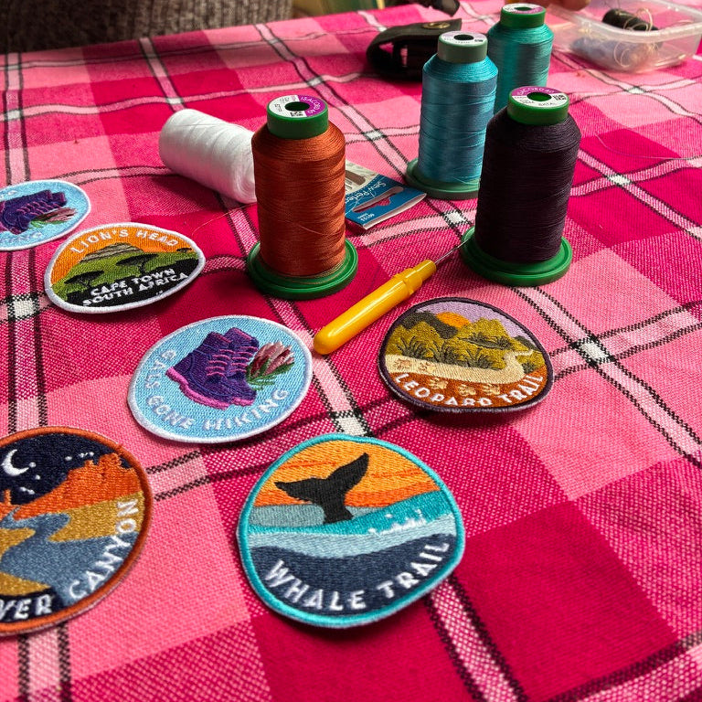 Colorful patches and spools of thread on a pink checkered tablecloth.