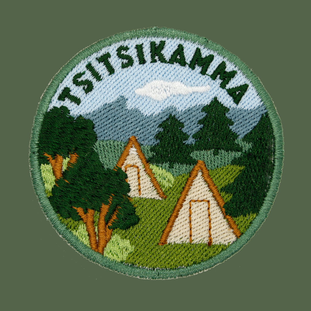 A circular embroidered patch featuring the word 'TSITSIKAMMA' arched over a landscape scene with mountains, trees, and two A-frame tents, shown on a solid dark green background.