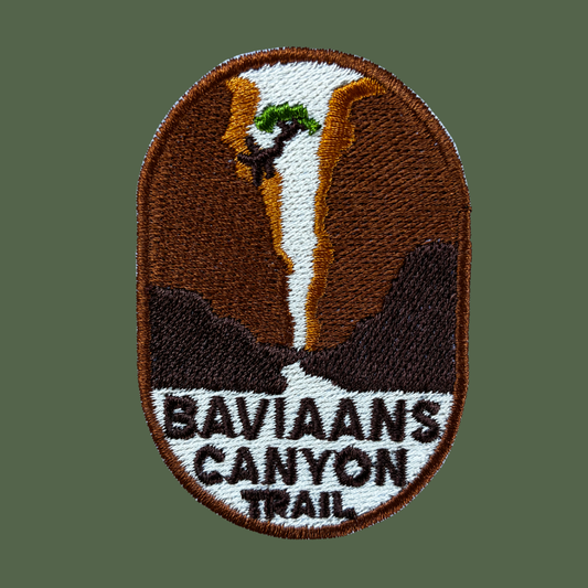 An oval embroidered patch featuring a canyon landscape with a waterfall and the text 'BAVIAANS CANYON TRAIL' on a muted green background.